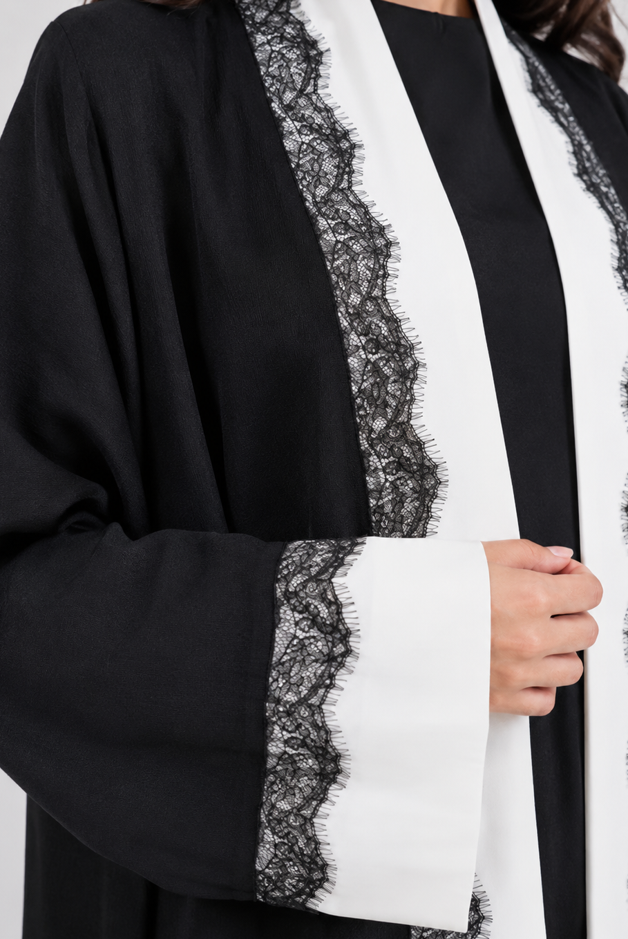A close-up of a black open-front robe or kimono-style garment with wide sleeves, featuring prominent white vertical panels and black lace trim along the edges and cuffs, worn over a black top.