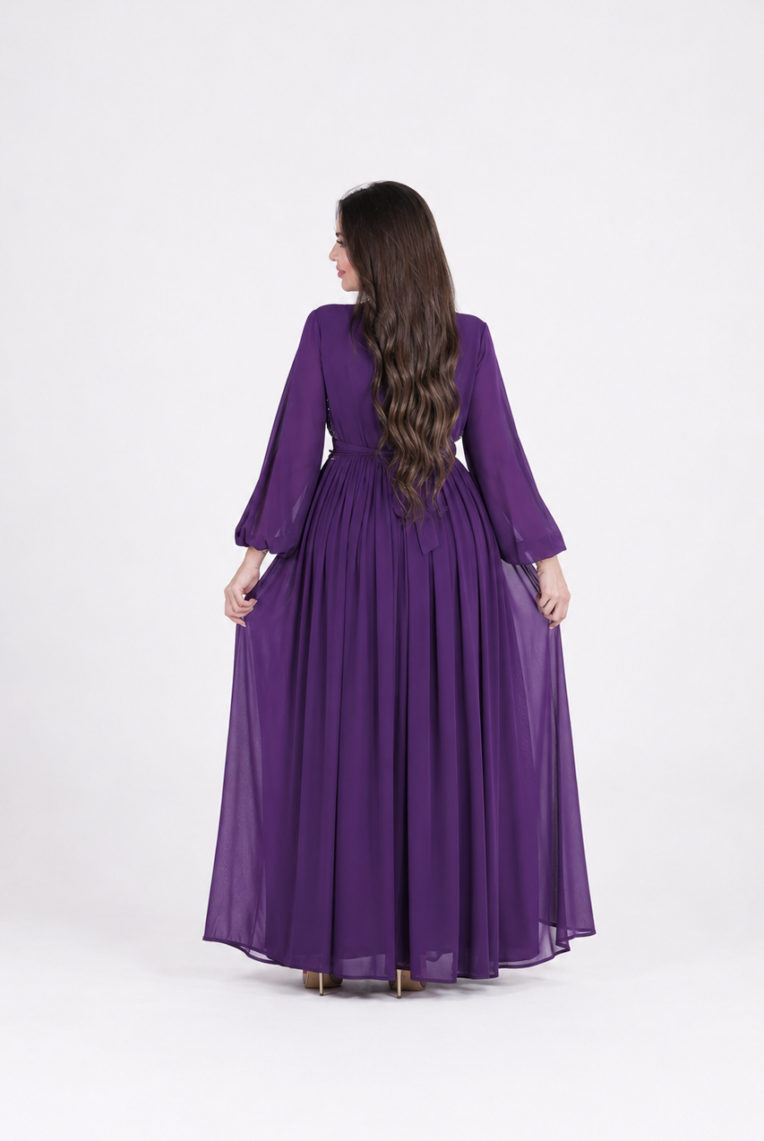 A woman viewed from behind wearing a long purple maxi dress with three-quarter sleeves and a gathered waist, standing against a plain light gray studio background.