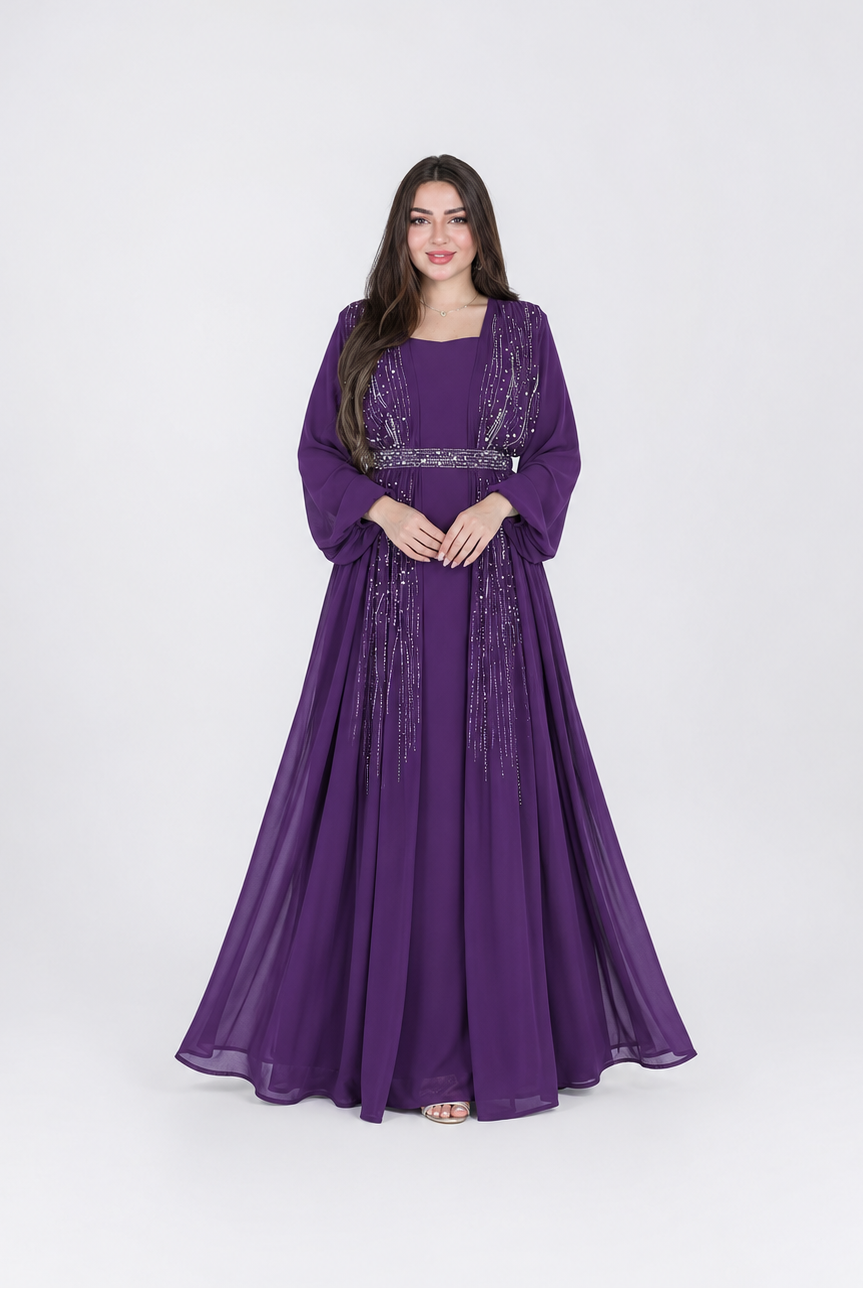 A woman modeling a floor-length purple gown with long sleeves, a square neckline, and silver beaded embellishments, standing against a light gray studio background.
