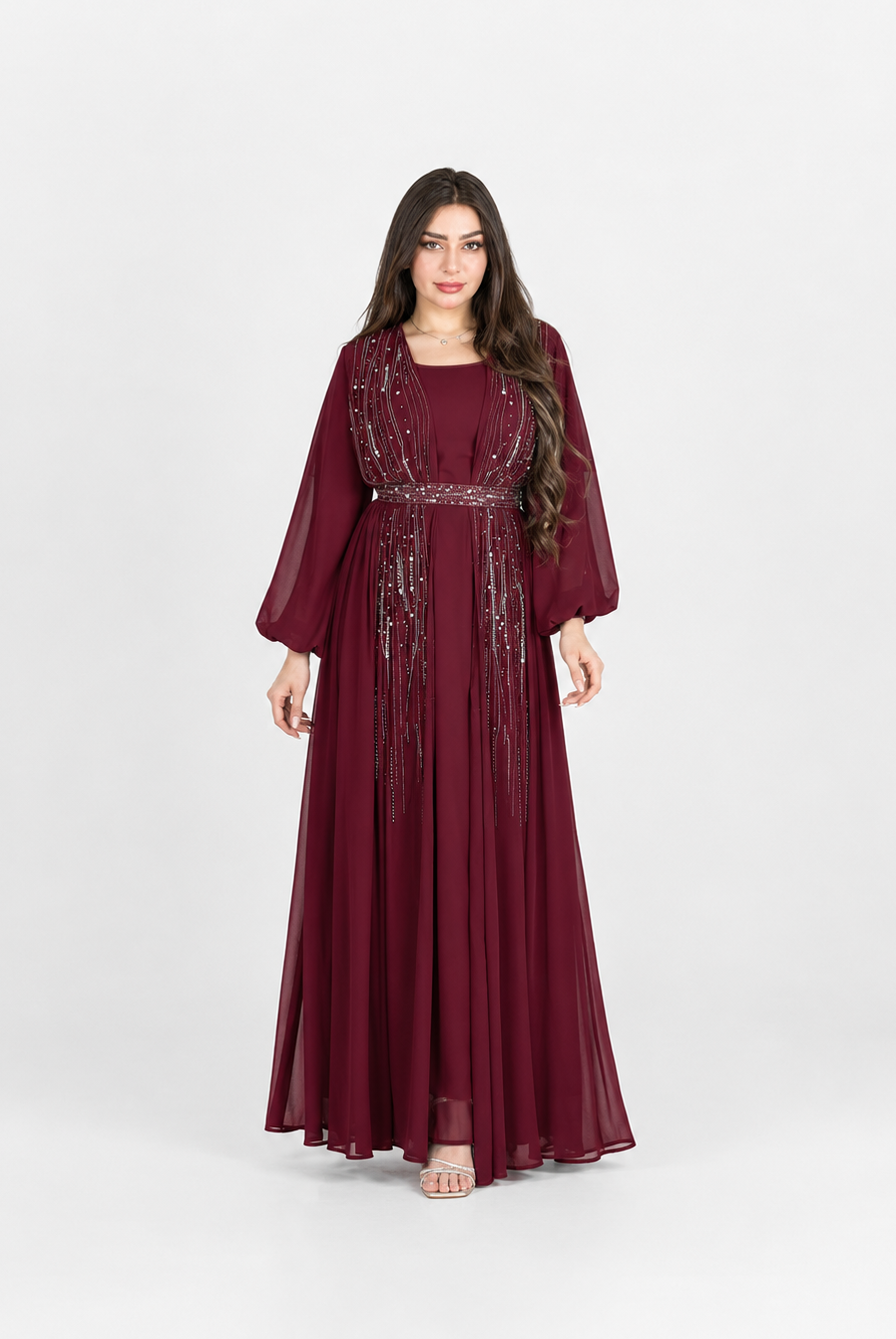 A woman modeling a long burgundy maxi dress with sheer three-quarter sleeves and silver sequin embellishments along the neckline and waist, photographed against a light gray studio background.