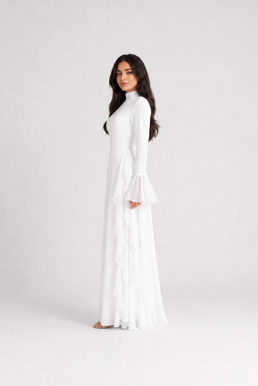 A woman modeling a long white maxi dress with long bell sleeves and a high neckline, standing against a plain light gray studio background.