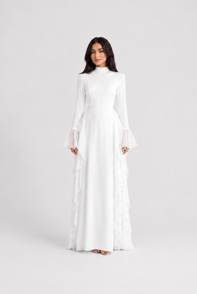 A woman modeling a long-sleeved white maxi dress with tiered ruffle details along the skirt, standing against a seamless light gray studio background.