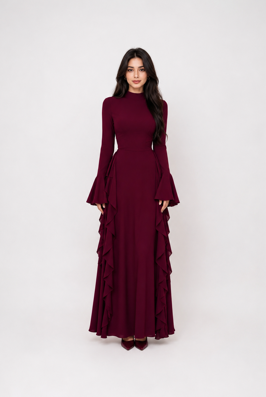 A woman modeling a long-sleeved, high-neck maxi dress in deep burgundy with dramatic ruffled layers on the skirt, set against a plain light gray studio background.