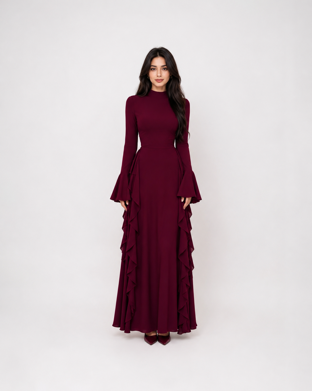A woman modeling a long-sleeved, high-neck maxi dress in deep burgundy with dramatic ruffled layers on the skirt, set against a plain light gray studio background.