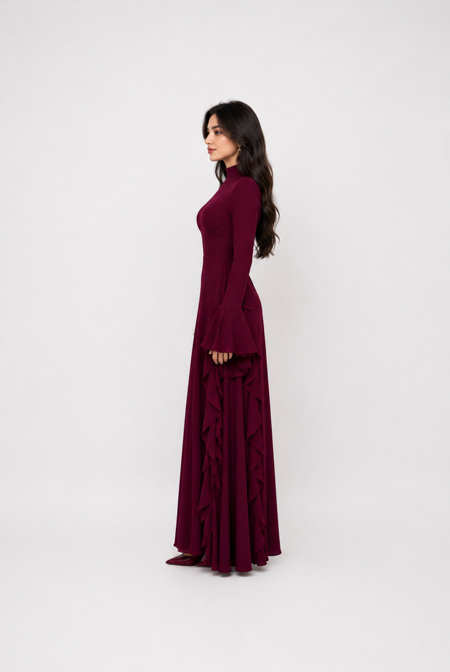 A woman modeling a long-sleeved, floor-length burgundy maxi dress in a side-profile view against a plain white studio background.