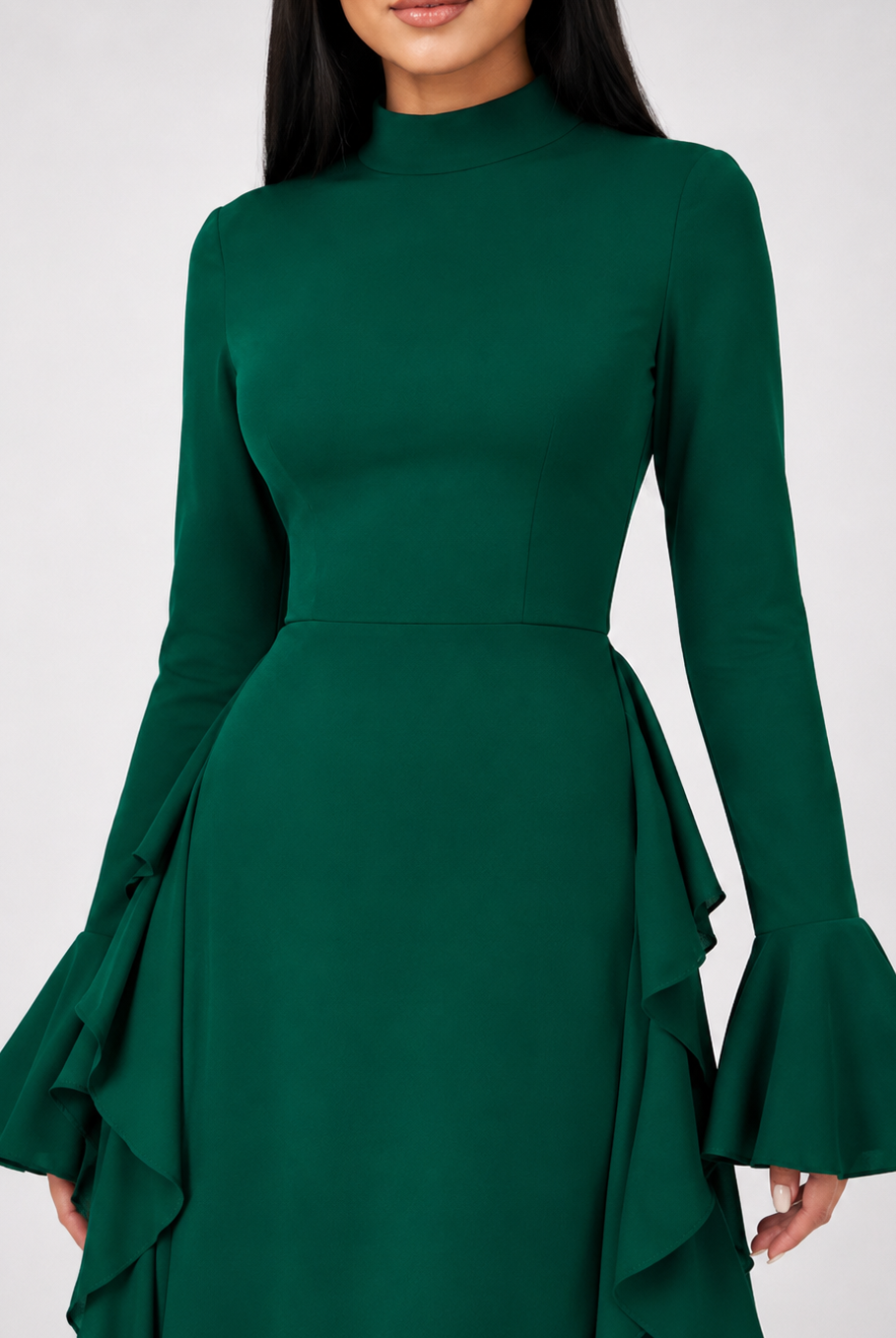 A woman wearing a dark green long-sleeve dress with a high mock neck, fitted waist, and dramatic flared ruffled bell sleeves, shown against a light gray studio background.