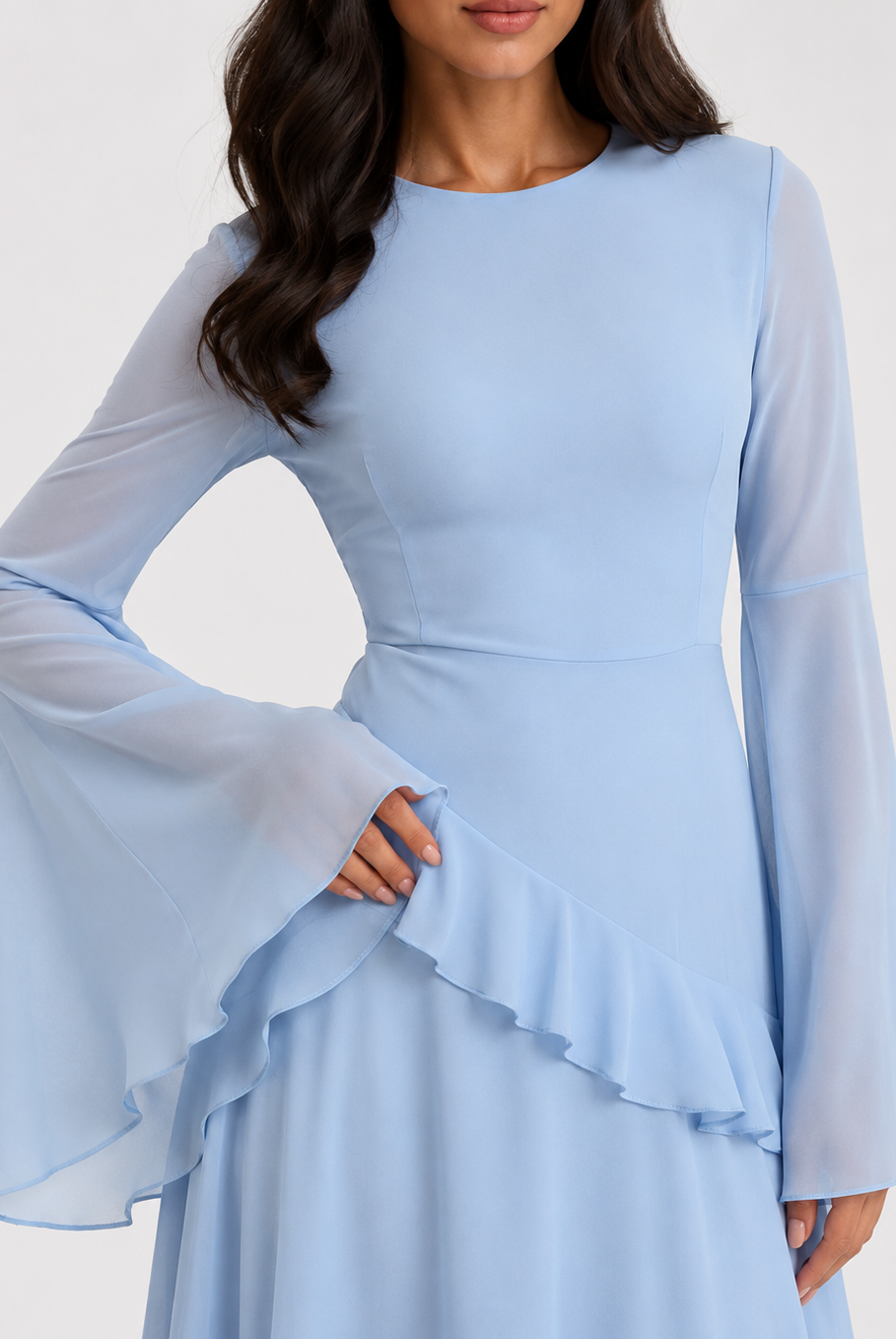 A woman wearing a light blue long-sleeve dress with sheer flared bell sleeves, a fitted waist, and a ruffled overlay detail on the skirt, shown against a plain light background.