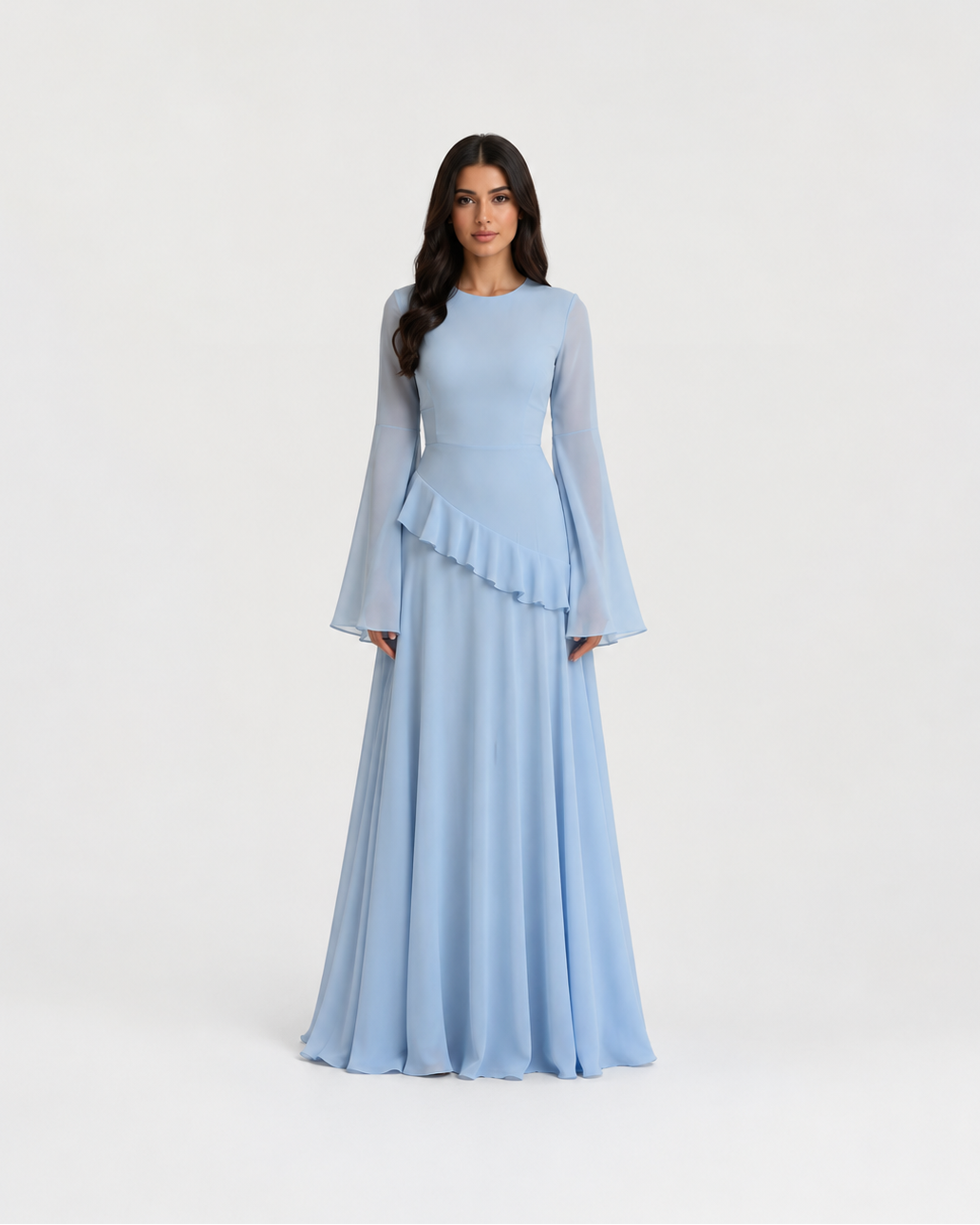 A woman modeling a light blue floor-length gown with long sheer bell sleeves, a round neckline, and a ruffled peplum waist, photographed against a plain light gray studio background.