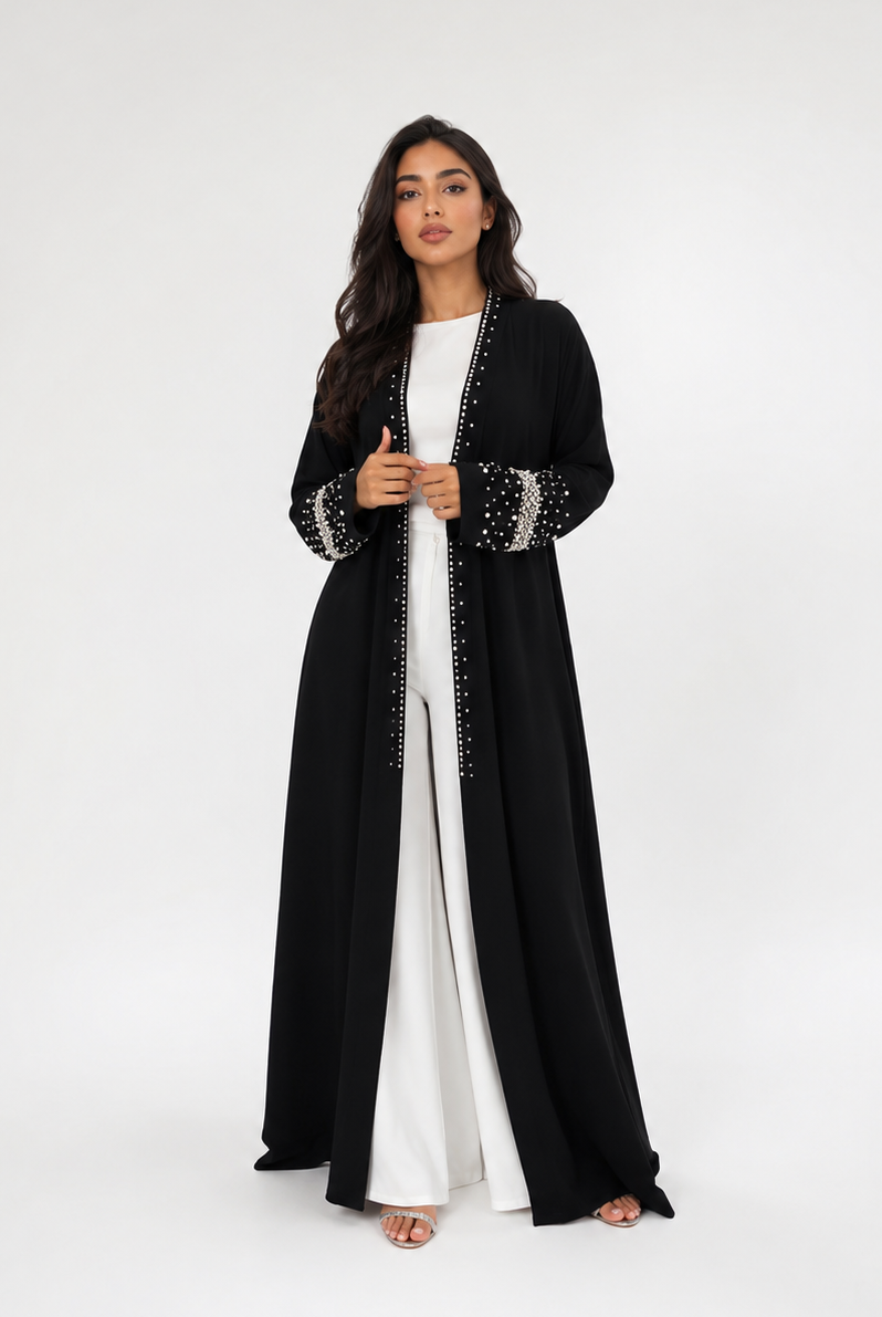 Woman wearing a black abaya with white trim on a white background