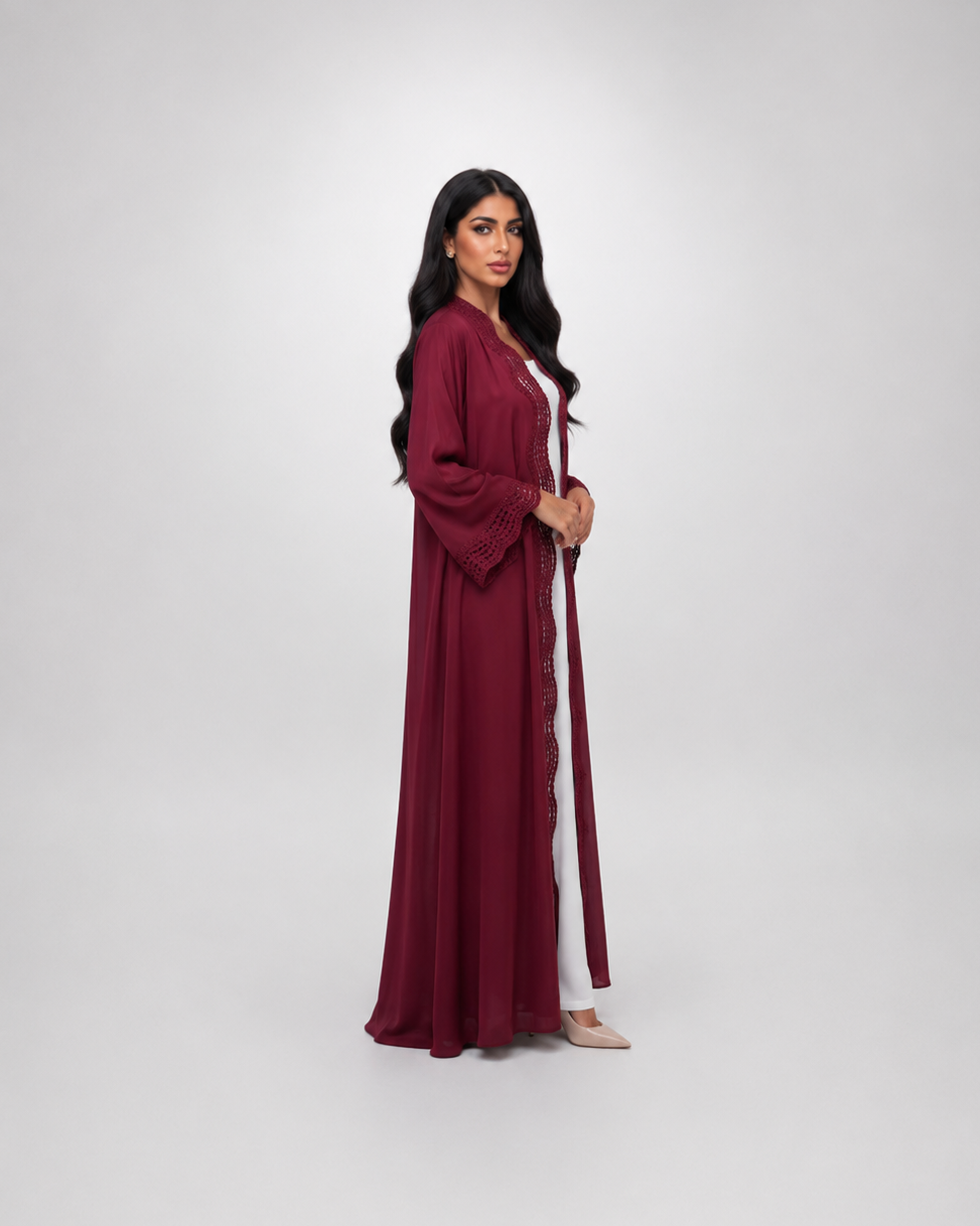 A woman modeling a long, flowing maroon abaya with a matching headscarf, standing against a light gray studio background.
