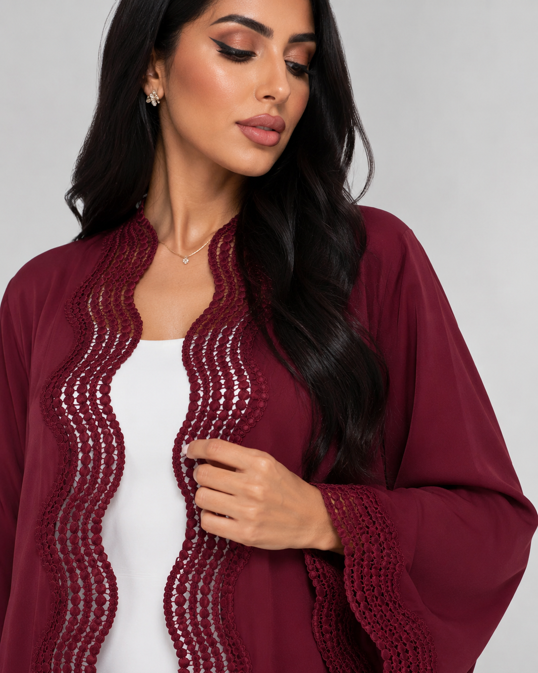 A woman wearing a burgundy open-front cardigan with wavy crochet trim over a white top, photographed against a light gray studio background.