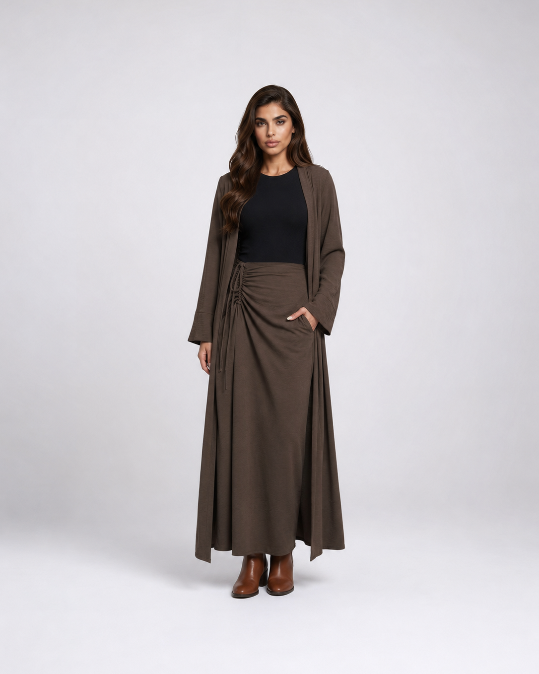 A woman modeling a dark brown long-sleeve wrap maxi skirt with a matching open-front cardigan, worn over a black top and brown ankle boots, against a light gray studio background.