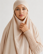 A woman wearing a light beige hijab and a matching long-sleeve top with a textured smocked sleeve, photographed against a clean light gray studio background.