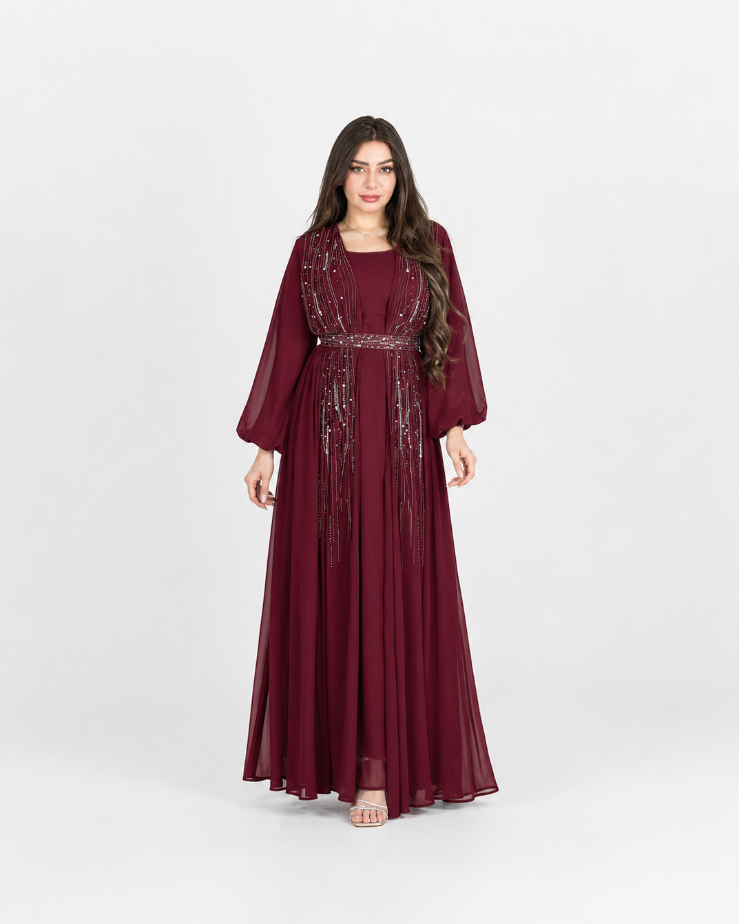 A woman modeling a long burgundy maxi dress with sheer three-quarter sleeves and silver sequin embellishments along the neckline and waist, photographed against a light gray studio background.