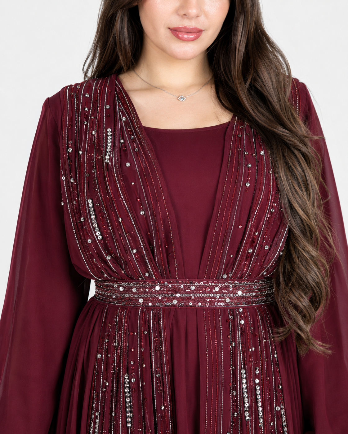 A close-up of a woman wearing a deep burgundy long-sleeve dress with silver beaded vertical stripes and a matching beaded waistband.
