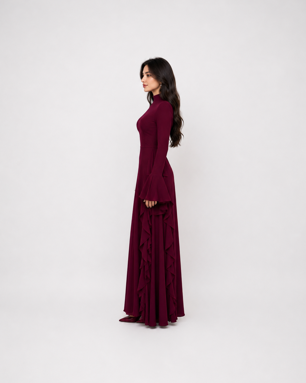 A woman modeling a long-sleeved, floor-length burgundy maxi dress in a side-profile view against a plain white studio background.