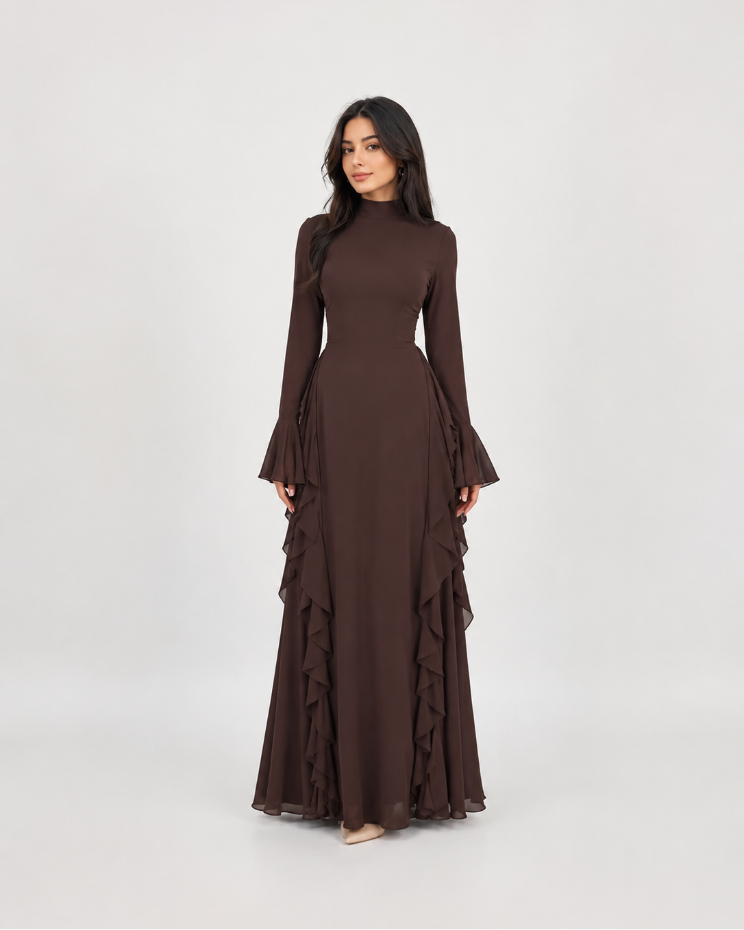 A woman modeling a long-sleeved, high-neck maxi dress in a solid dark brown color, featuring flared bell sleeves and a tiered ruffle skirt, set against a plain light gray studio background.