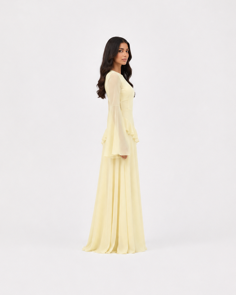 A woman modeling a long-sleeved, floor-length pale yellow dress, shown from the back against a seamless white studio background.