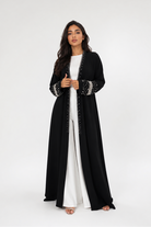 Woman wearing a black abaya with white trim on a white background