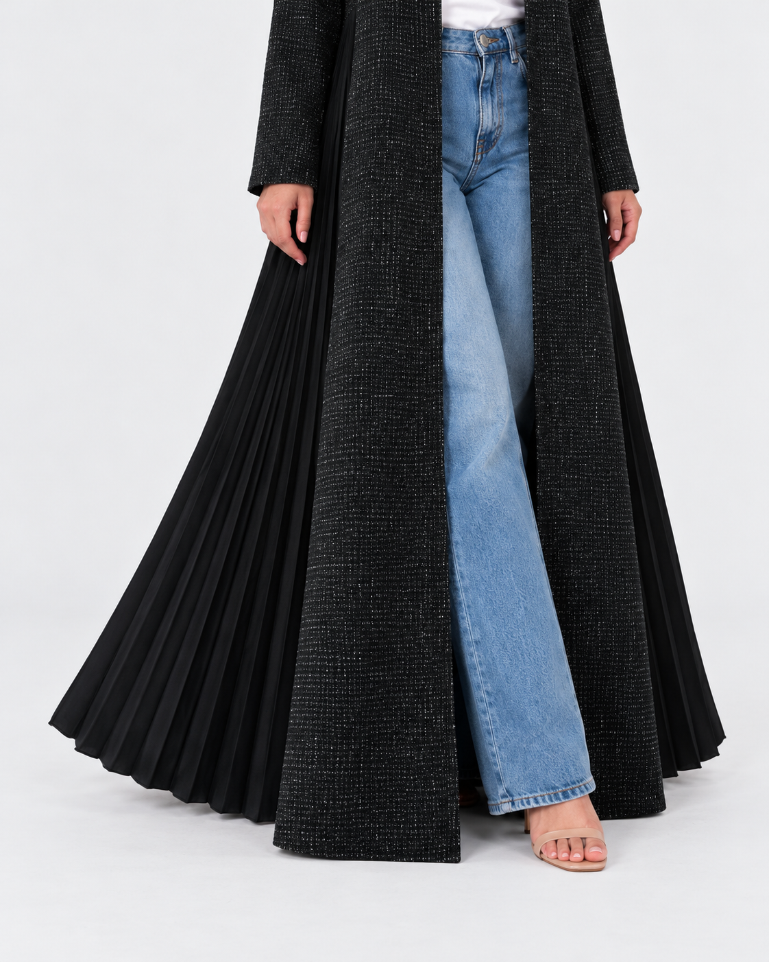 A long black pleated open-front coat or duster worn over light blue wide-leg jeans, shown on a model against a light gray studio background.