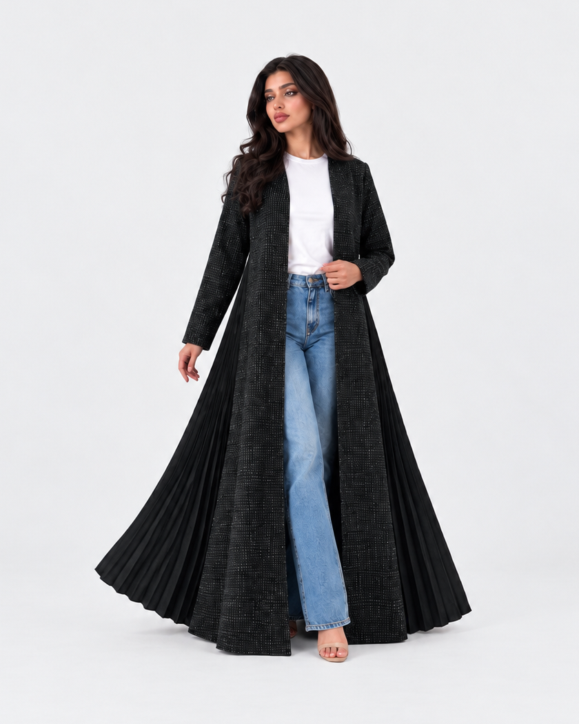 A woman modeling a long, open-front black textured coat over a white top and light blue jeans, standing against a plain light gray studio background.
