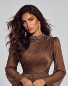 A woman modeling a brown sheer long-sleeve top with a pleated bodice, embellished collar, and scalloped beaded hem, paired with a white skirt against a light gray studio background.