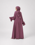 A woman wearing a long, flowing mauve-purple abaya with matching hijab, shown from the back against a light gray studio background.