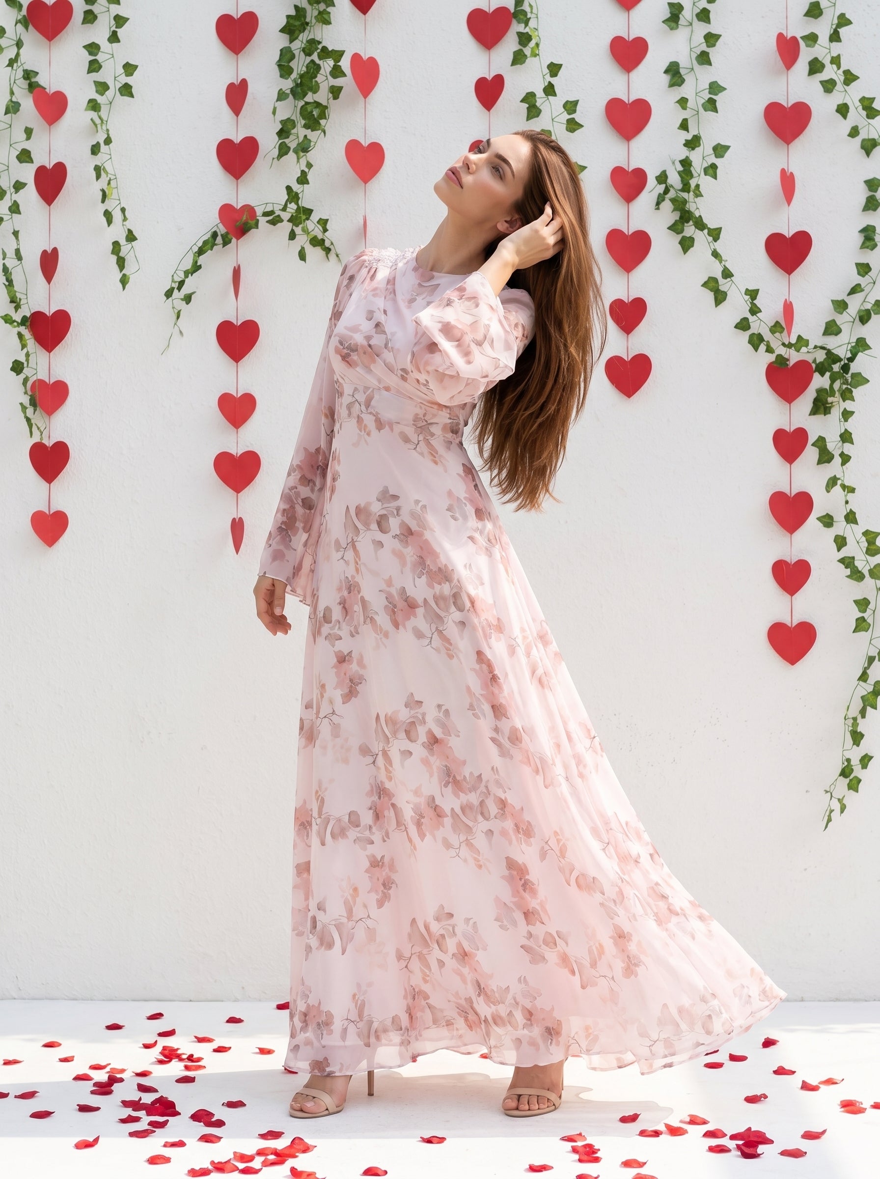 Woman in a floral dress standing among heart-shaped decorations on a white wall.